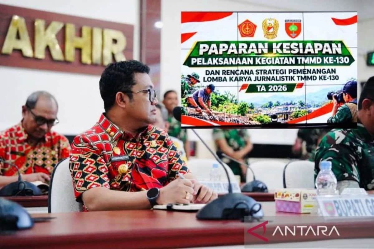 Darmawangsyah Muin duduk di meja rapat dengan layar paparan kesiapan TMMD ke-130 di belakangnya