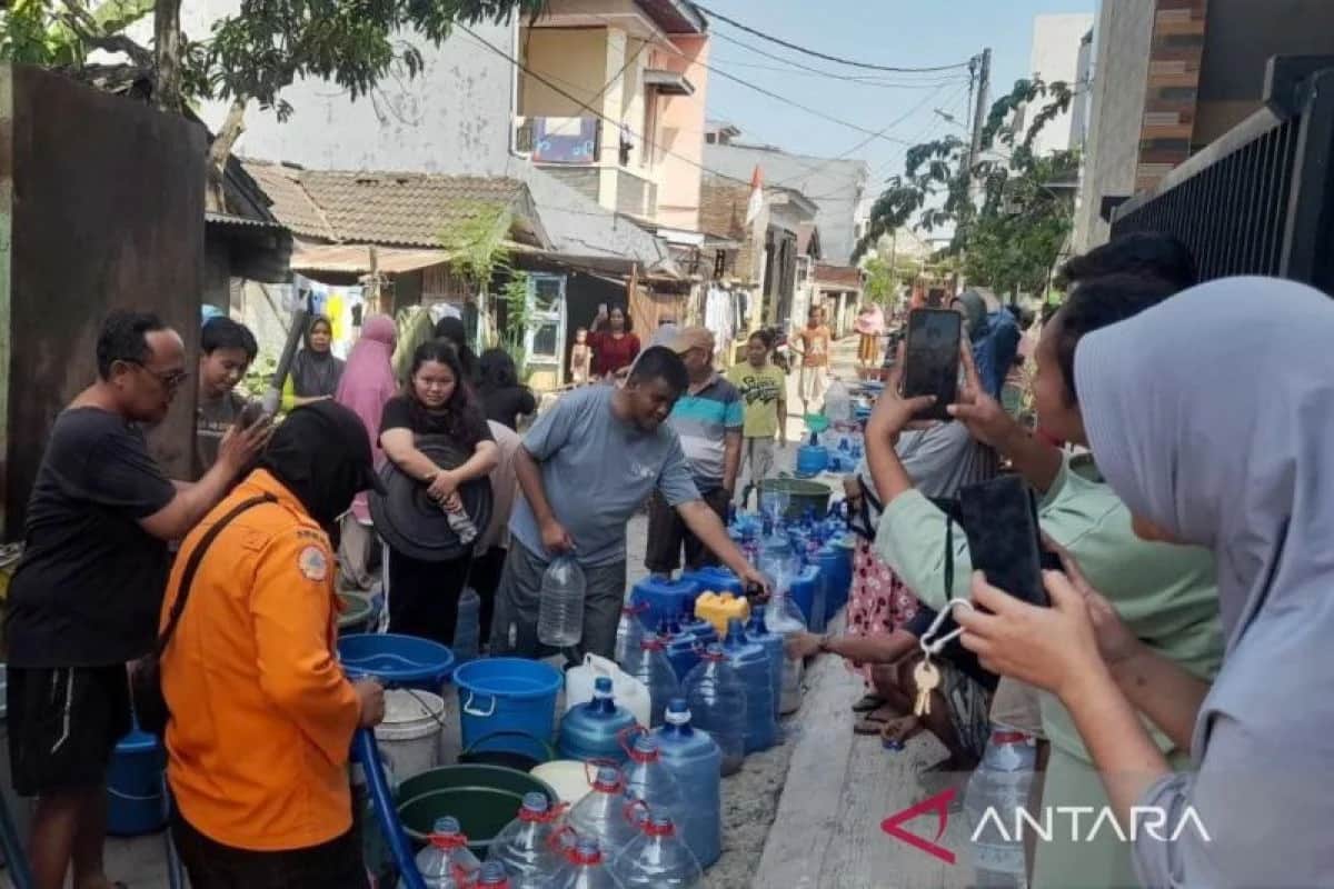 Warga dan petugas berada di lorong permukiman dengan galon dan ember untuk menampung air