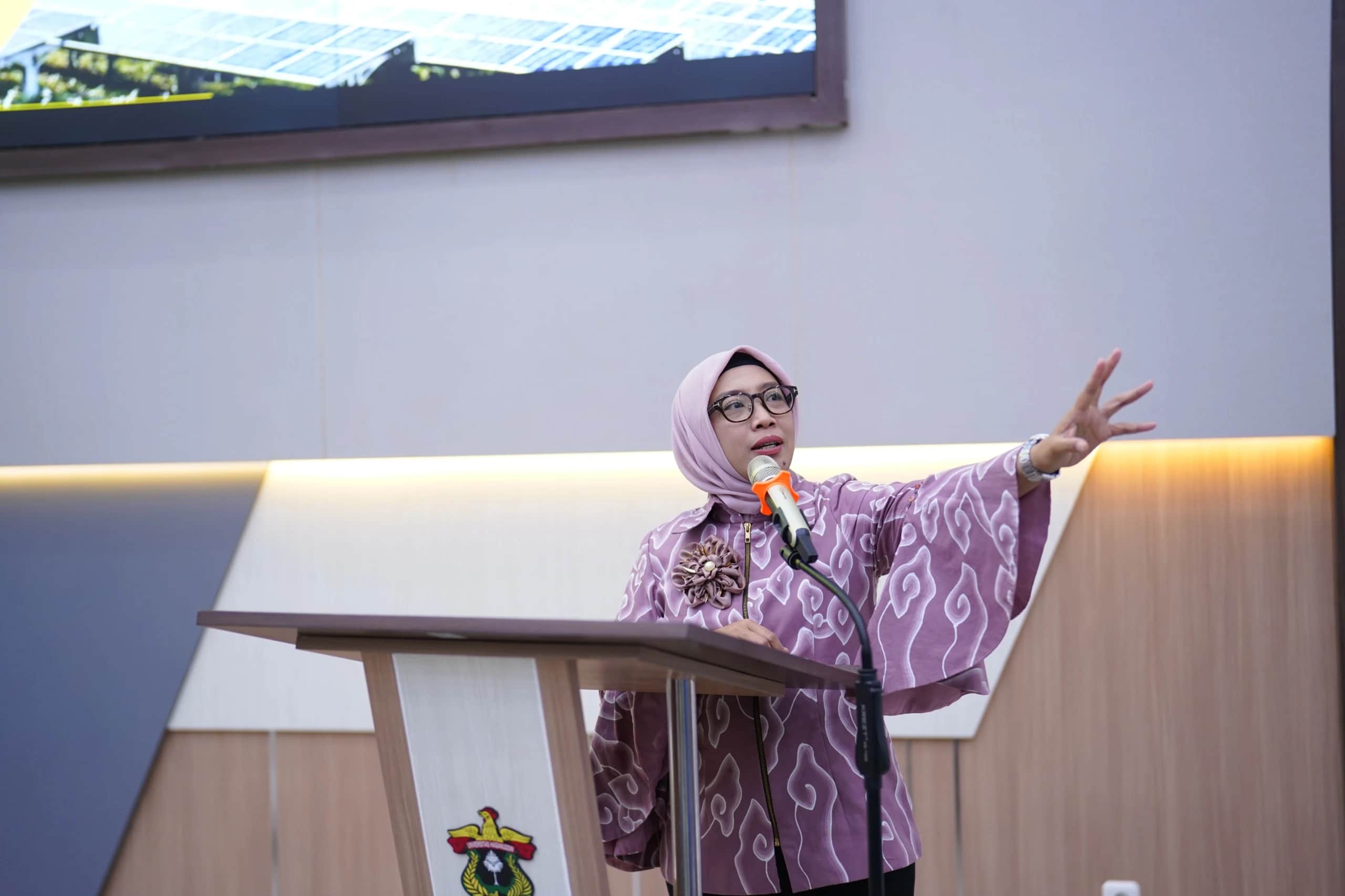 Eniya Listiani Dewi berbicara di podium berlogo Universitas Hasanuddin dengan layar panel surya di belakangnya