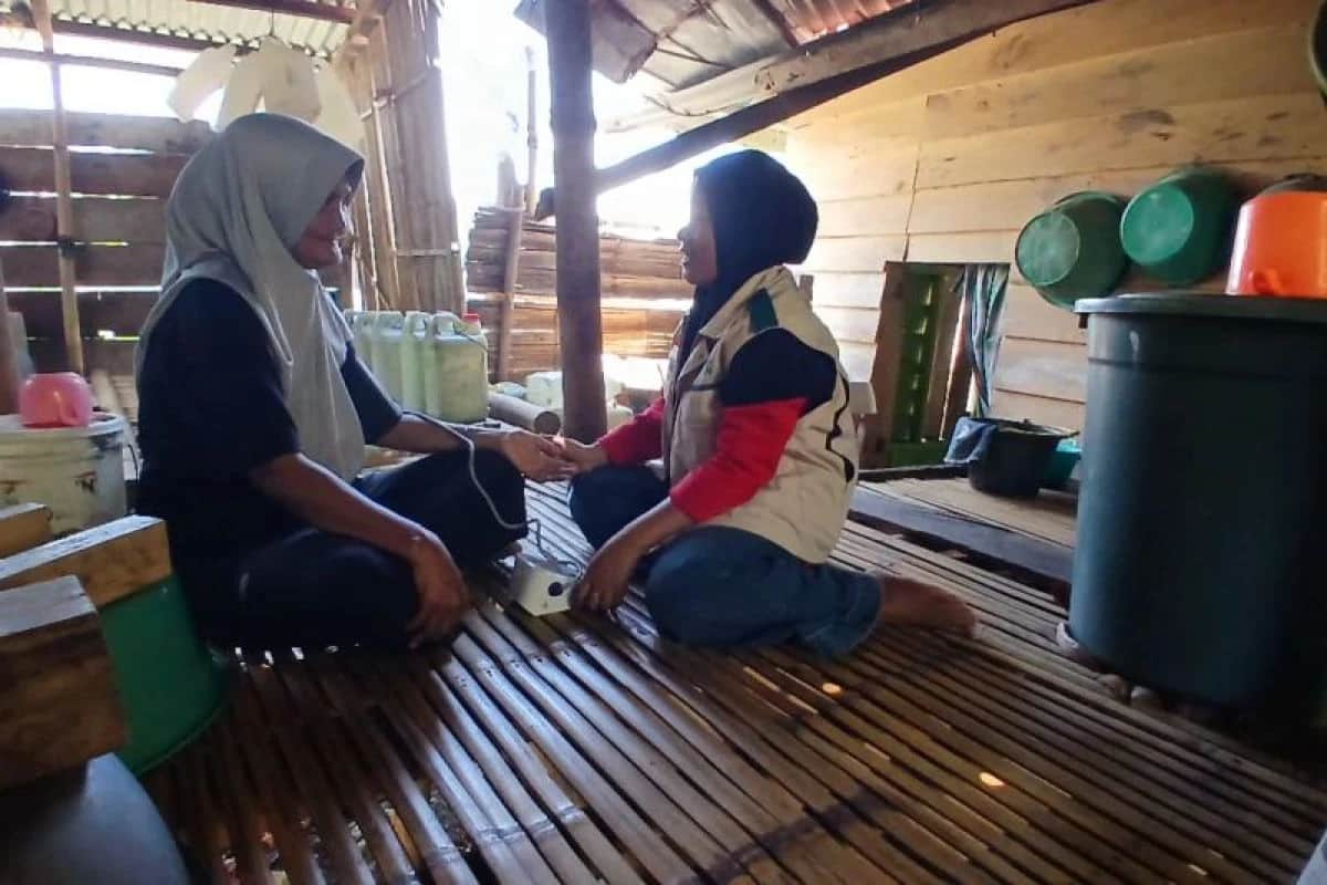 Petugas berompi memeriksa tekanan darah seorang warga yang duduk di dalam rumah kayu