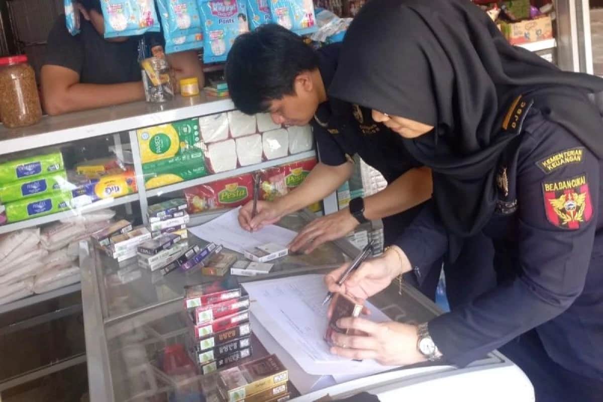Dua petugas Bea Cukai mencatat informasi kemasan rokok di etalase toko